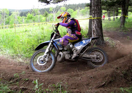 A woman coming around a corner on a dirt bike. 