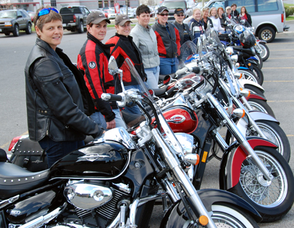 Women in a line standing beside their motorcycles