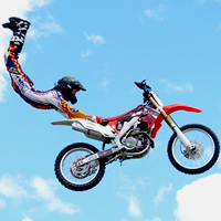 A man in the air hanging onto the seat of a motorbike. 