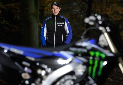 A young man standing behind a blue dirt bike. 