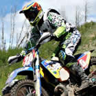 Photo of a guy riding a dirt bike over a large mound of dirt. 