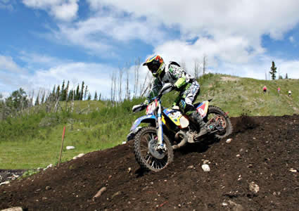 Photo of a guy riding a dirt bike over a large mound of dirt. 