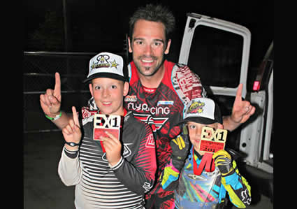 photo of a father and his two sons standing together and smiling while they are holding up their index fingers to indicate number 1. 