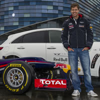 Two men standing beside a grand prix car and a white car. 