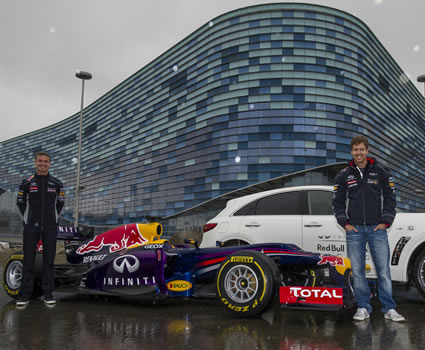 Two men standing beside a grand prix car and a white car. 