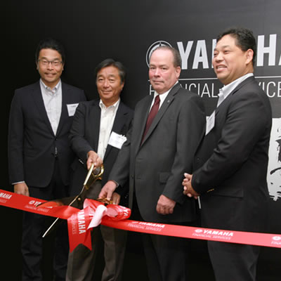 Yamaha officials cutting a red ribbon. 