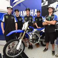 Six young men standing around a new blue dirt bike on the podium. 